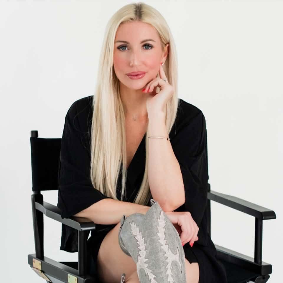Monica Shepherd, founder of Barnstar Aesthetics, in a black dress and silver cowboy boots, seated in a director's chair